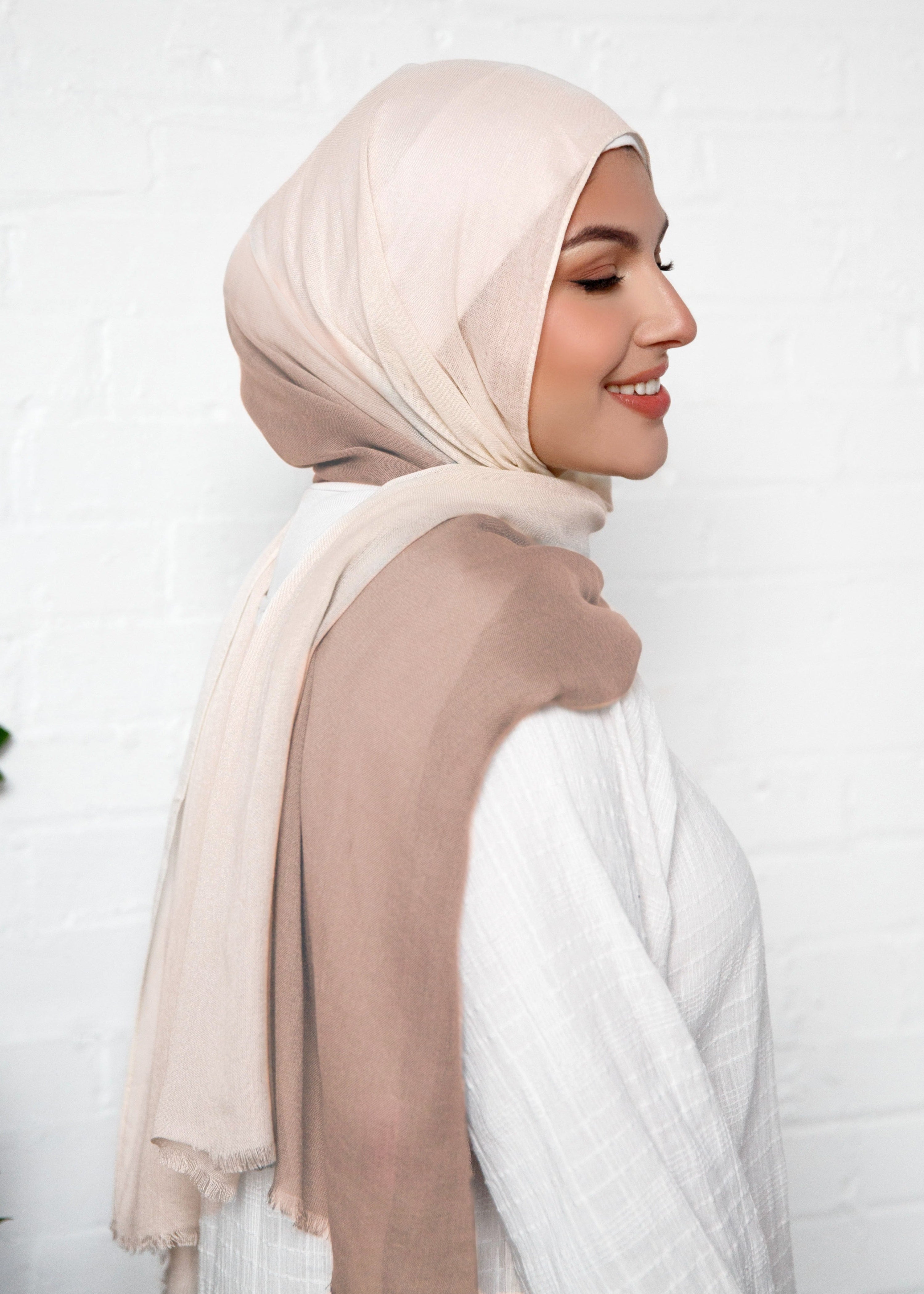 Woman wearing a beige hijab and white top against a white background