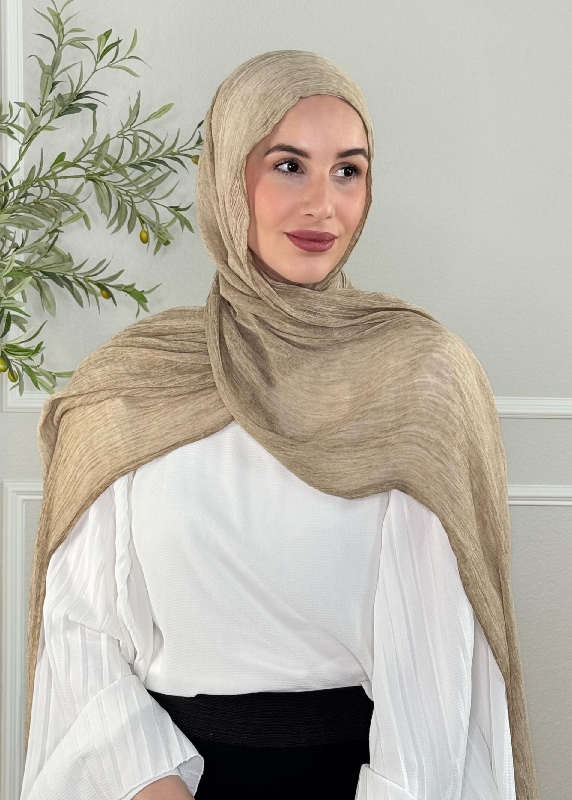 Woman wearing a beige hijab and white blouse against a neutral background