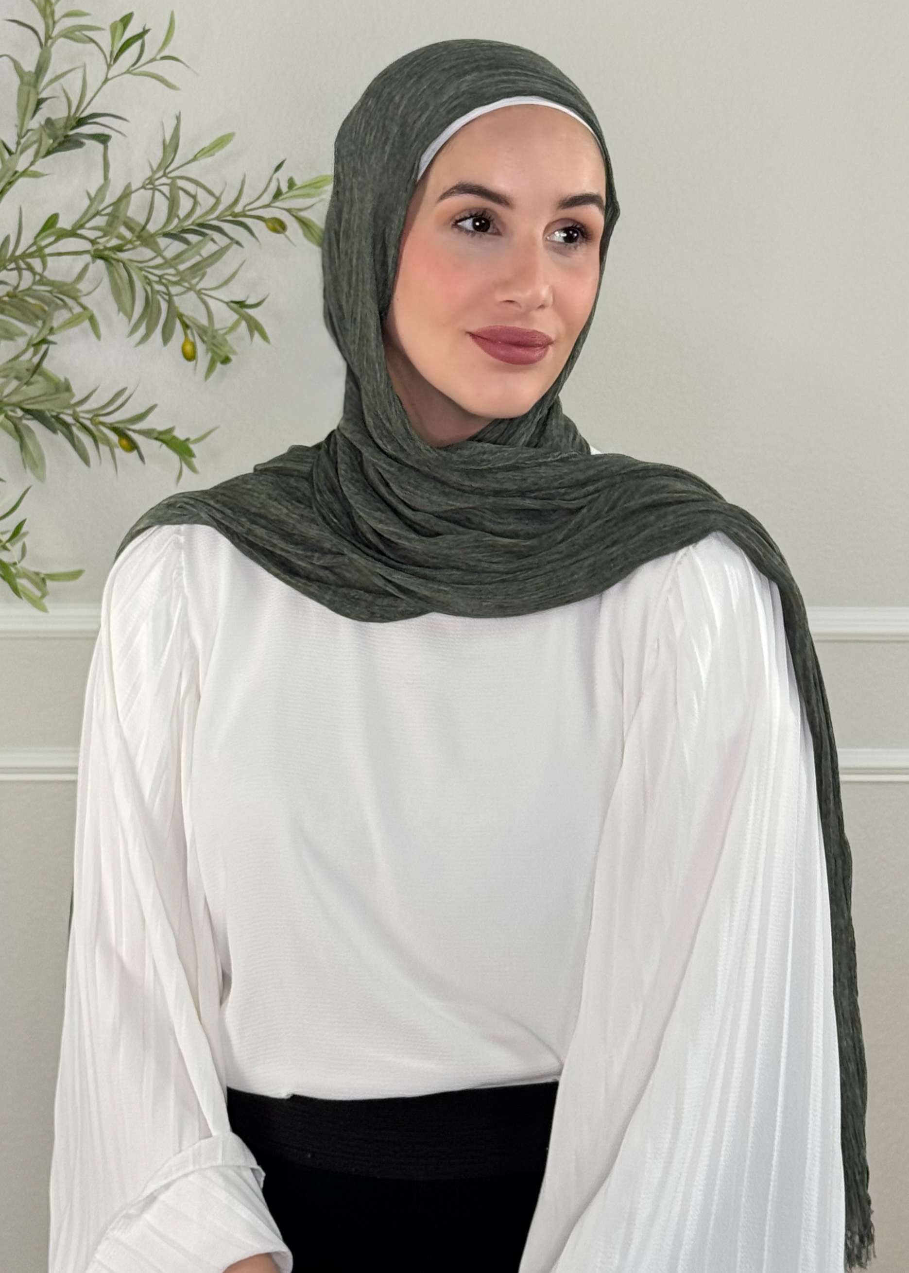 Woman wearing a green hijab and white blouse against a neutral background