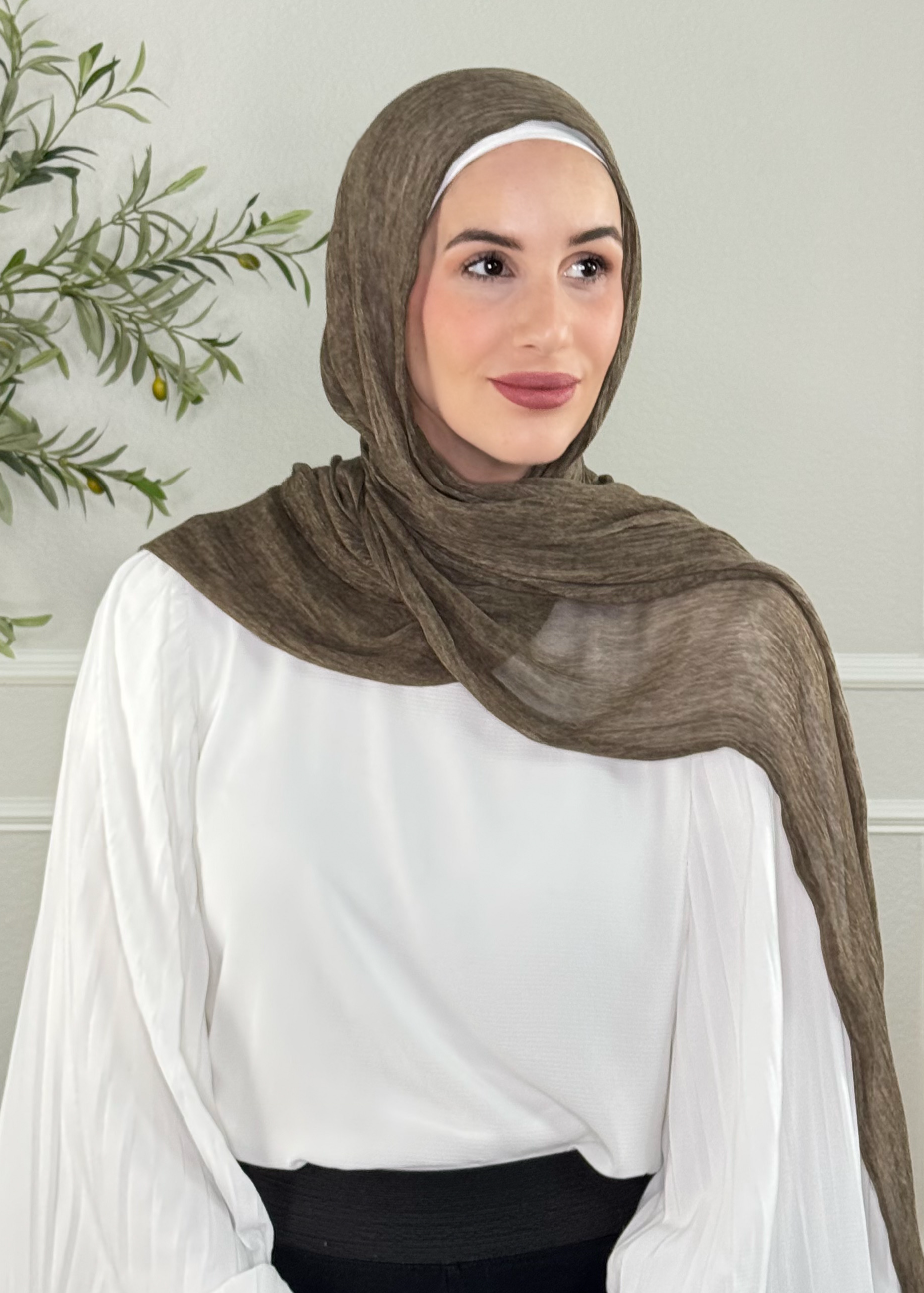 Woman wearing a brown hijab and white blouse in a neutral setting