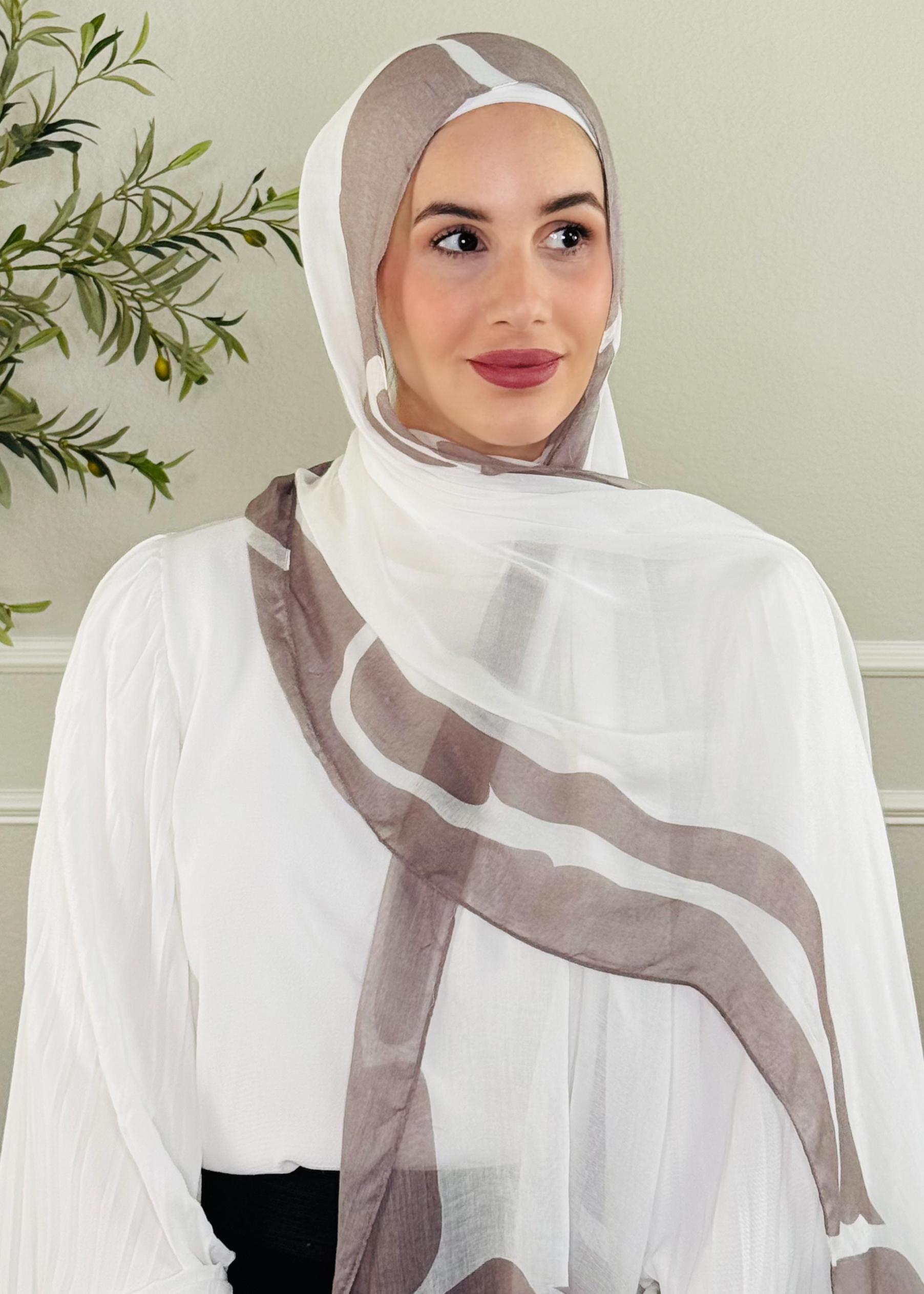 Woman wearing a white hijab with brown stripes against a neutral wall.