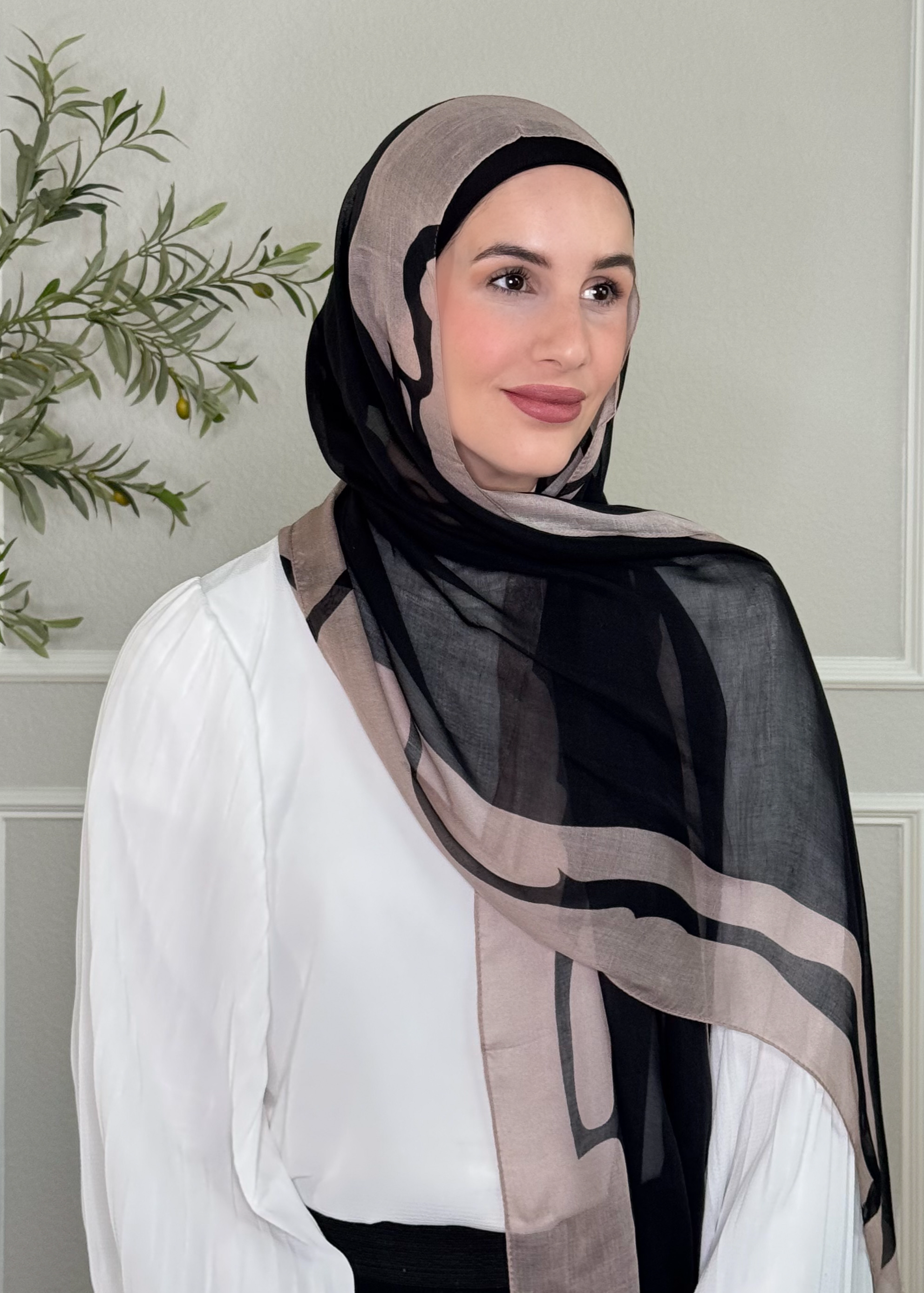Woman wearing a black and beige hijab with a white blouse against a neutral background