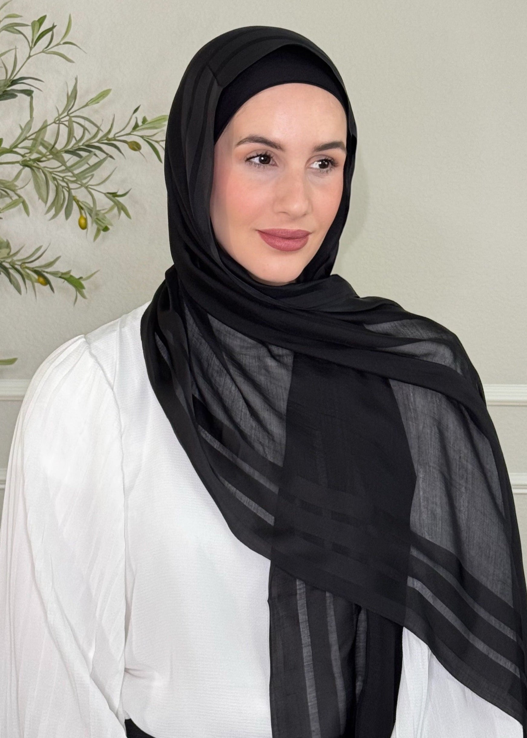 Woman wearing a black hijab and white top in a neutral setting