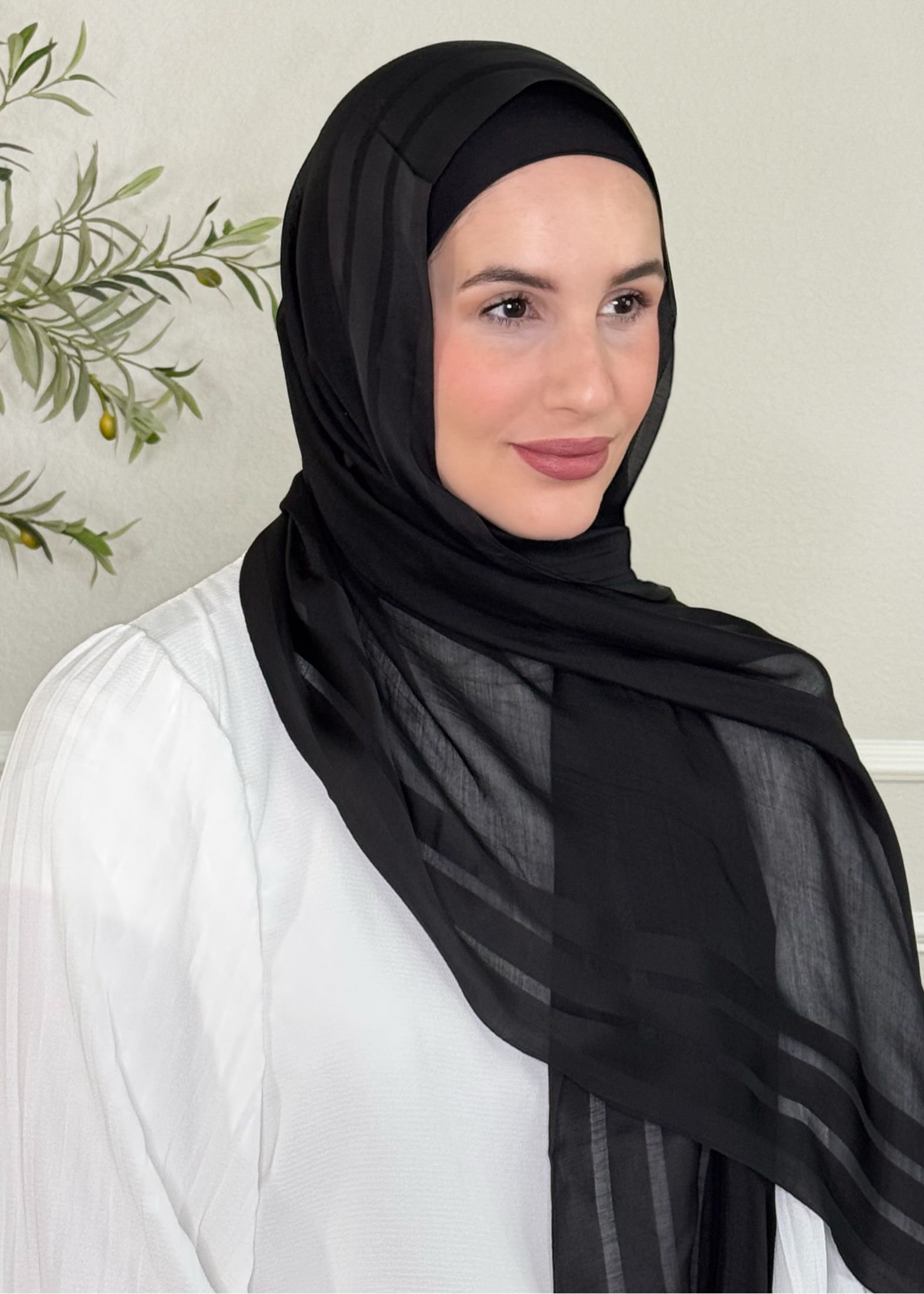 Woman wearing a black hijab and white outfit in a neutral setting