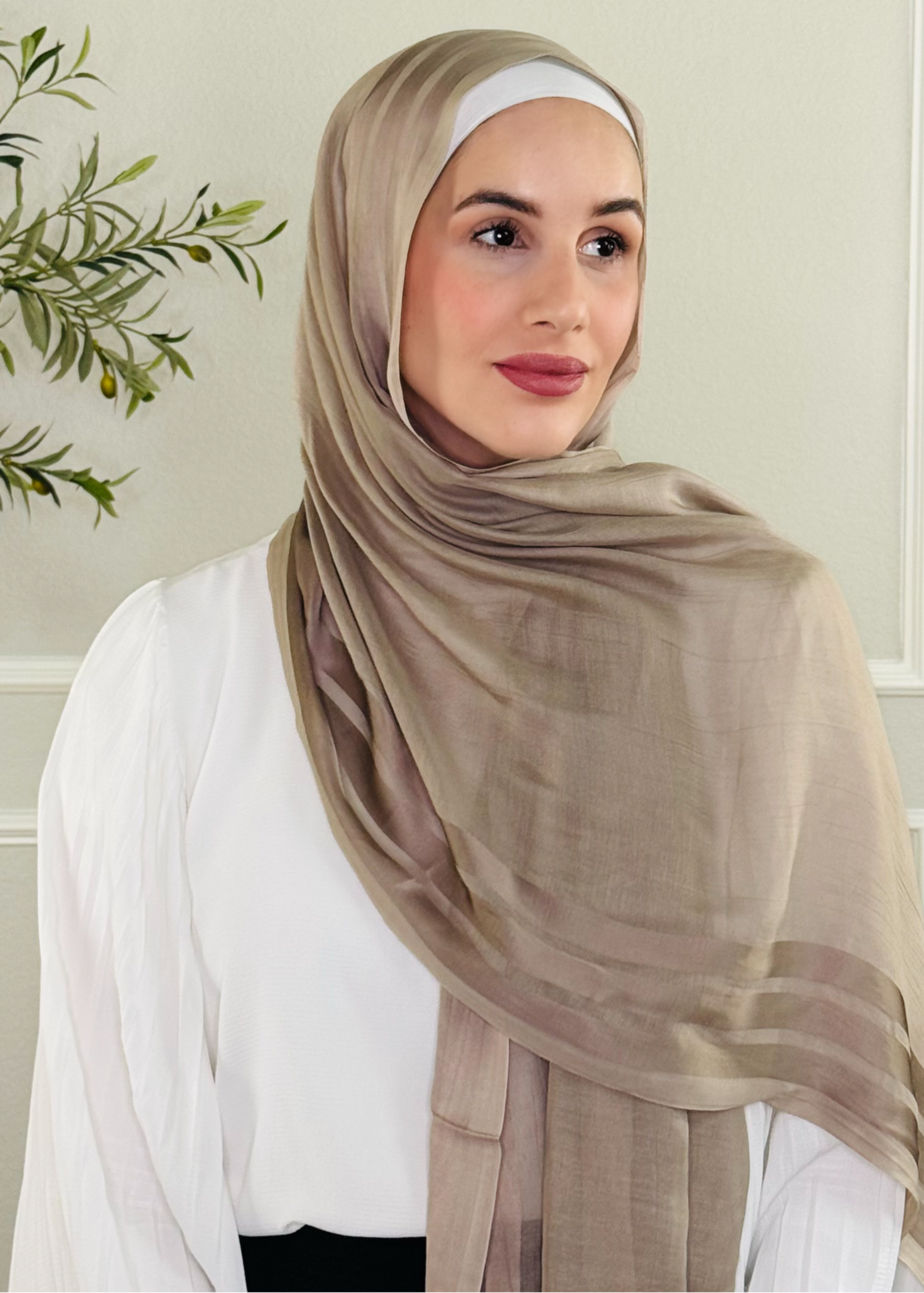 Woman wearing a beige hijab in a room with a plant in the background