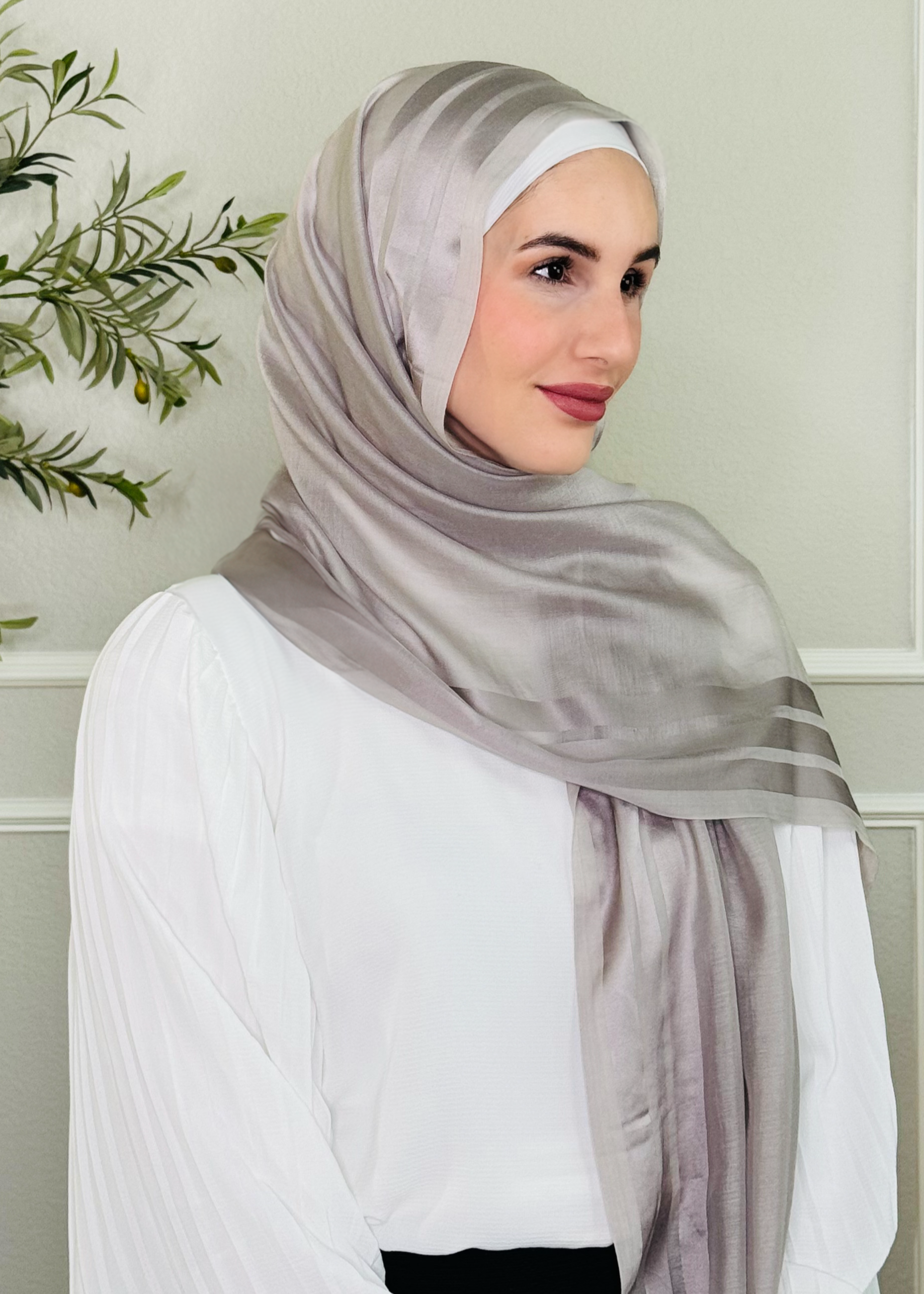 Woman wearing a gray hijab in a minimalistic setting with a plant.